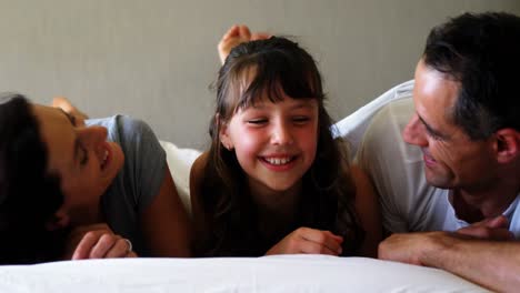 Parents-kissing-their-daughter-on-cheek-in-bedroom