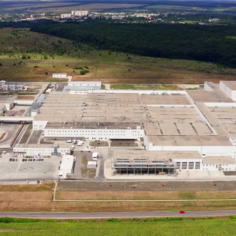 Huge plant on field. Modern industrial complex surrounded by rural nature. Camera rising and moving back. Aerial view