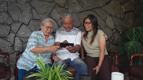familia asiática alegre con padres ancianos e hija adulta viendo video en el teléfono inteligente juntos en casa
