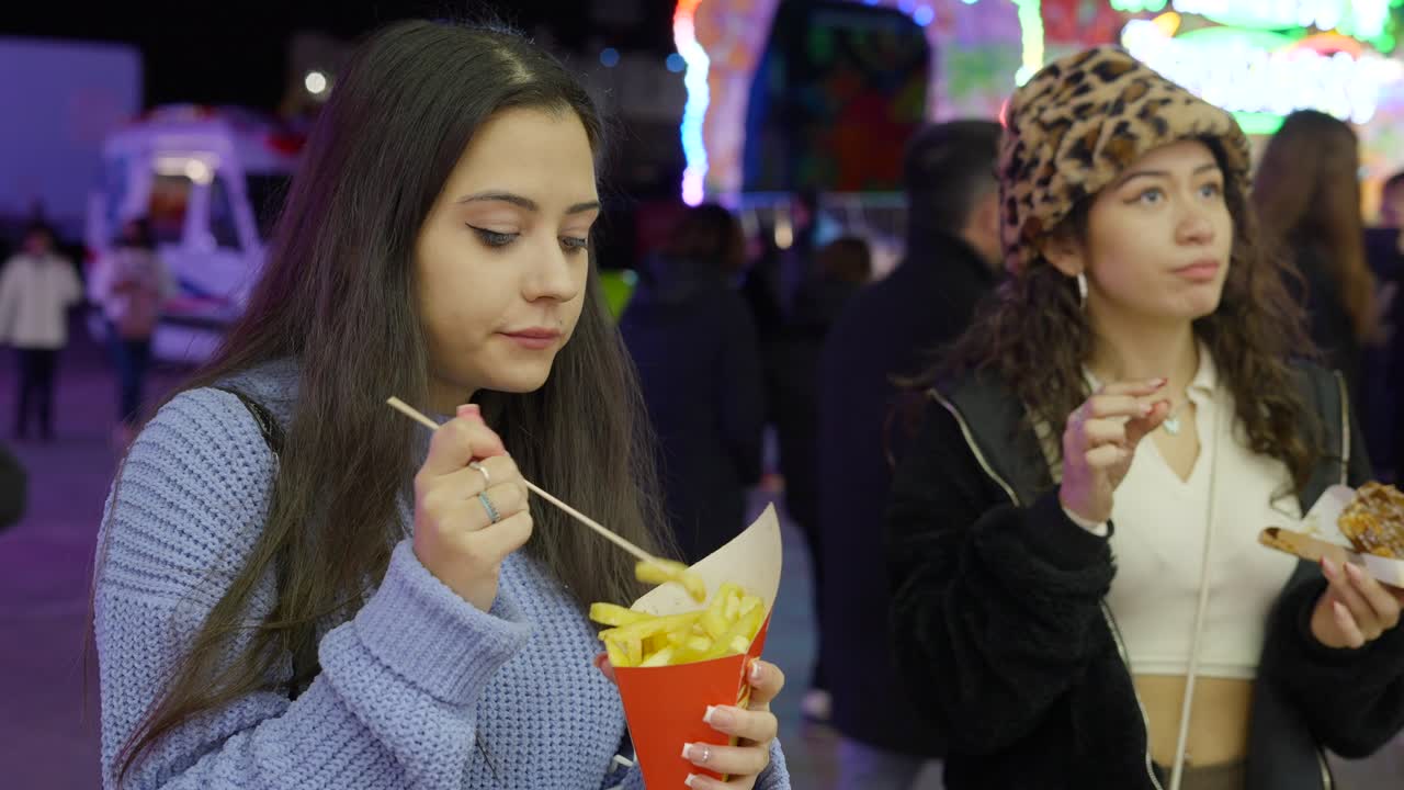Two young women eating fries at a festival