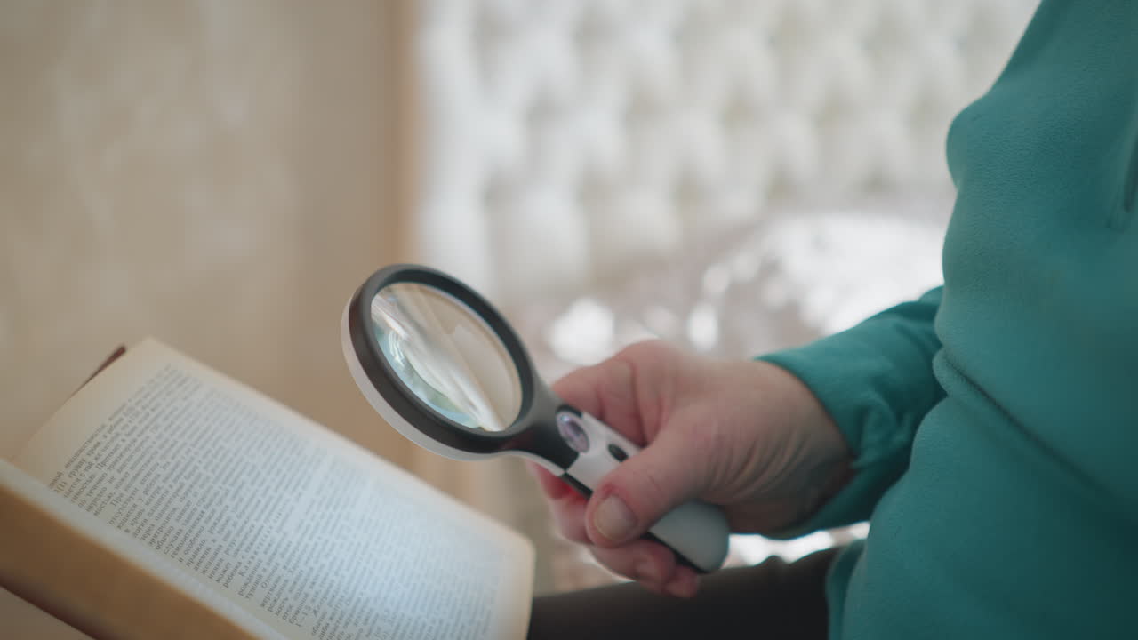 Senior woman reading book with magnifying glass, carefully examining text. Bright, cozy indoor setting with soft natural light illuminating pages, enhancing readability