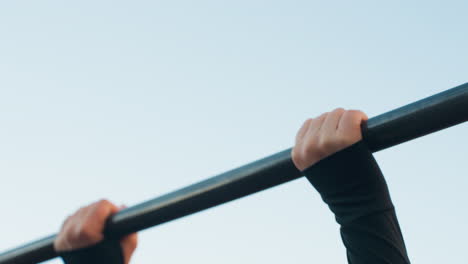 sky view of female hands gripping horizontal bar for balance against pale blue sky conveying focus strength and stability during urban outdoor workout preparation showcasing fitness routine