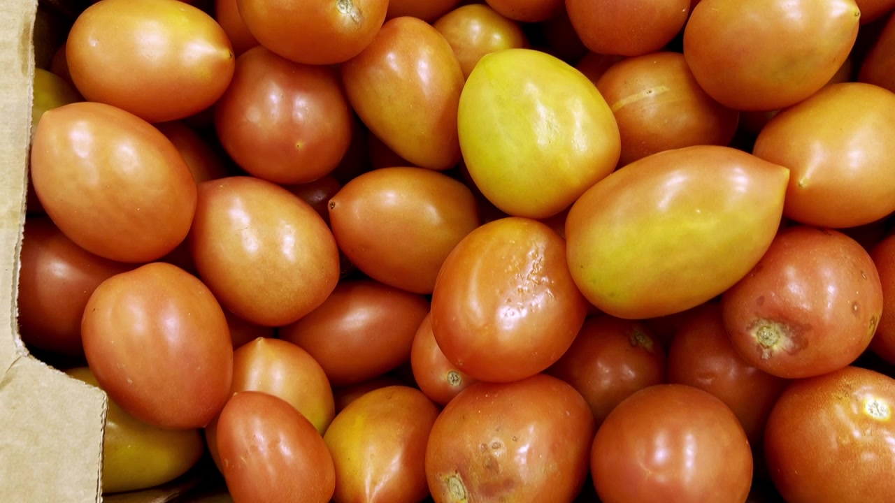 Nærbillede af modne Roma-tomater pænt pakket i papkasser, der viser deres glatte tekstur og levende røde farve på et marked