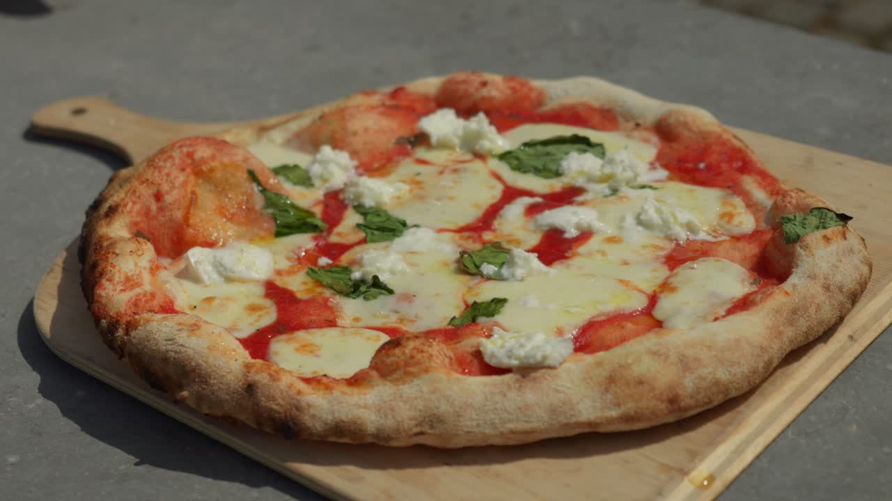 Inquadratura media di pizza gourmet servita su un tagliere di legno all'aperto in una giornata di sole