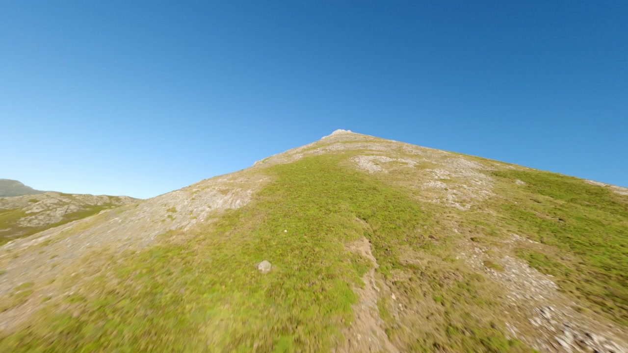 Ripresa aerea dinamica con drone FPV che sorvola una lussureggiante cresta montuosa verde sotto un cielo azzurro limpido a Isoba, Leon. Perfetto per progetti di viaggio, natura e sostenibilità