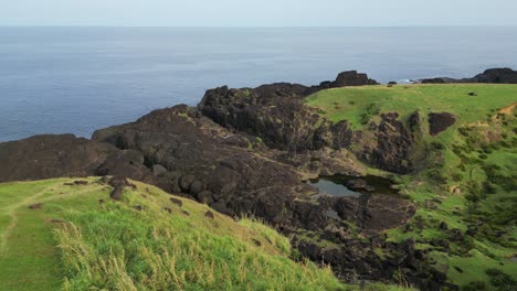 scenic aerial view of rocky, oceanfront cliff with grassy hills and turquoise waters