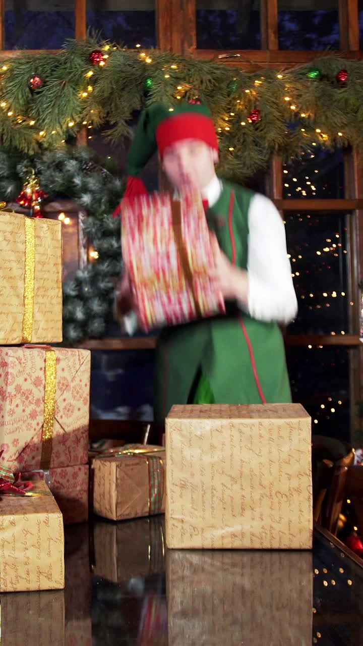 Presents for xmas holidays. Cheerful elves putting gift boxes on the table near Christmas tree in decorated room. Vertical video