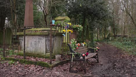 gravestone decorated with flowers in remembrance of a loved one, covered in moss in a forest graveyard on a cloudy day