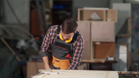 Un-Hombre-Atractivo-Con-Uniforme-De-Trabajo-Quita-La-Abrazadera-Y-Sopla-El-Polvo-De-Un-Producto-De-Madera