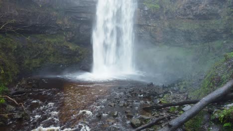 aerial of big waterfall with chopped logs and cave behind the water in wales uk 4k