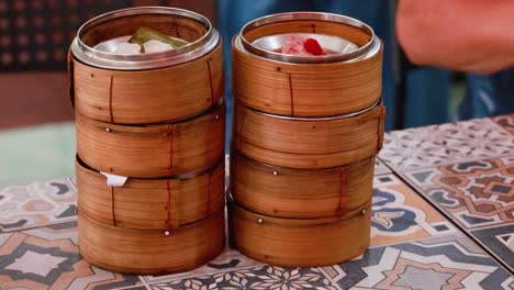 hands arrange bamboo steamers filled with dim sum on a patterned table in phuket, thailand. bright lighting enhances the vibrant setting