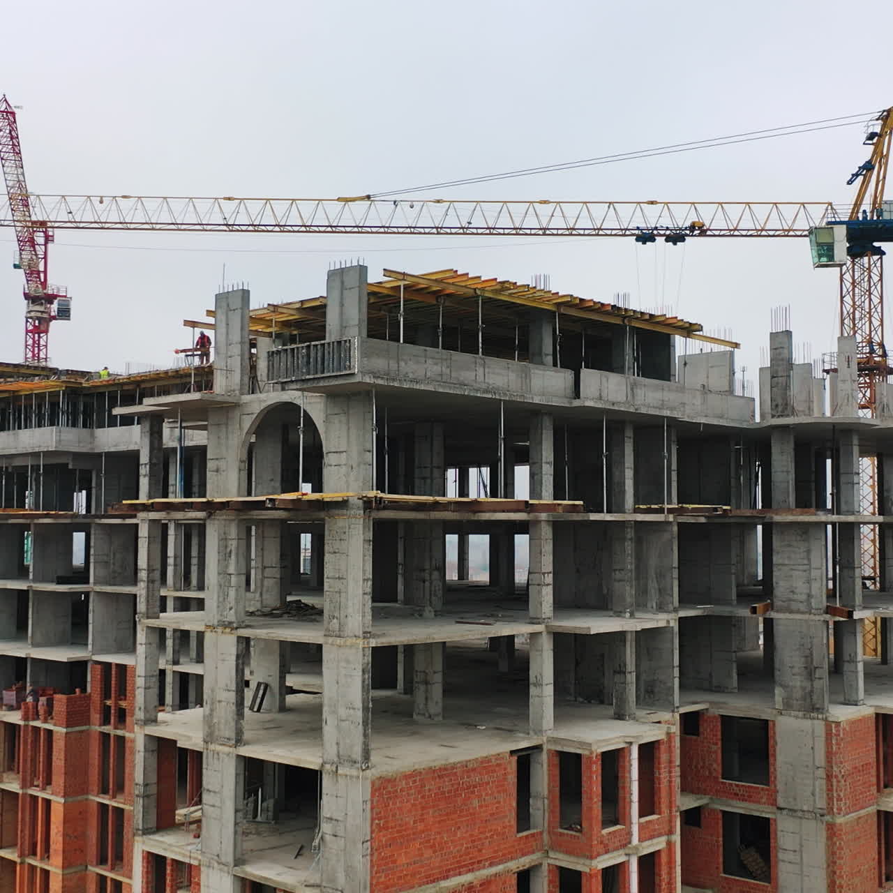 Process of construction high-rise building. Labor workers on a big construction site on the background of working crane in the city. Slow motion. Camera moves top down.