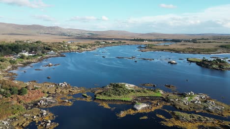 Dolly-Aéreo-Filmado-Hacia-Atrás-Sobre-El-Pintoresco-Lago-Connemara-En-Galway,-Irlanda,-Con-Vistas-Al-Lago-Azul-Reflectante,-Terreno-Abierto-Con-Colinas-Onduladas-Y-Colinas-Con-Vegetación-En-Un-Día-Soleado