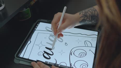 a woman designer with long red hair traces cursive letters on a tablet to prepare the pattern for a tattoo