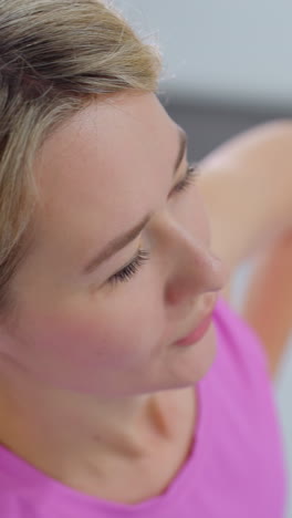 primer plano de una mujer con ropa deportiva rosa con la mano en la cintura ajustando la postura mientras mira a un amigo en el fondo, los detalles borrosos muestran a otra persona también ajustando el movimiento en la sesión de fitness