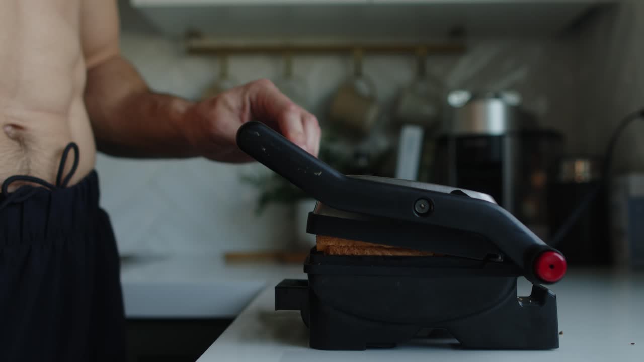 un hombre con el pecho desnudo hace sándwiches calientes en una parrilla de sándwich