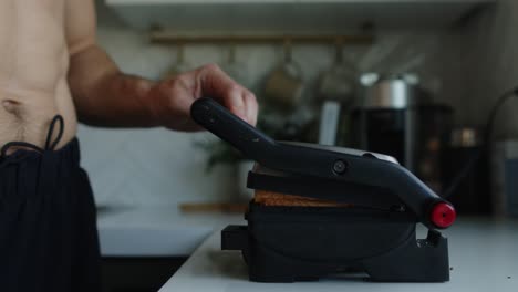 ein mann mit nackter brust macht heiße sandwiches in einem sandwichgrill