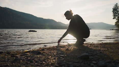 lady squats stroking water of lake at sunset. woman searches inner harmony during solo journey and dreaming about future. calm atmosphere at twilight enhances experience