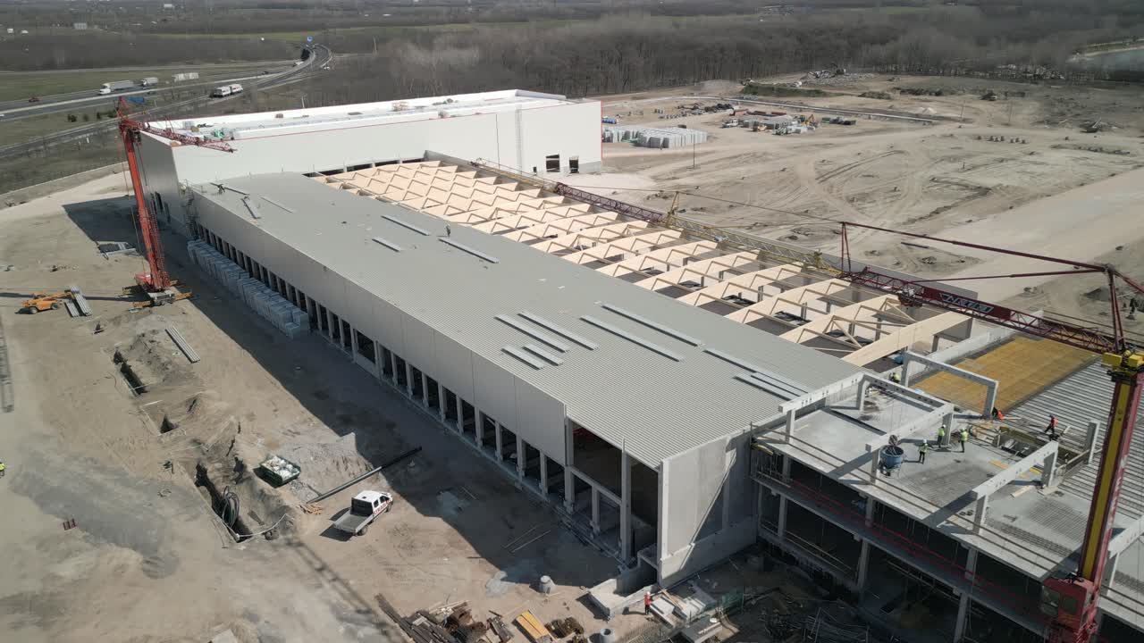 Drone shot of a large warehouse being built, showing structural work and surrounding industrial area