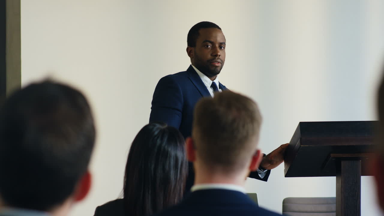 Rear view of people sitting in a conference room who are listening to a African American businessman talking confidently and emotionally