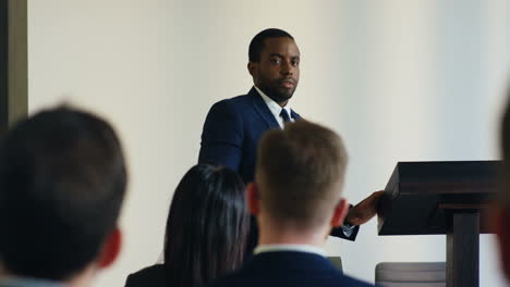 rear view of people sitting in a conference room who are listening to a african american businessman talking confidently and emotionally