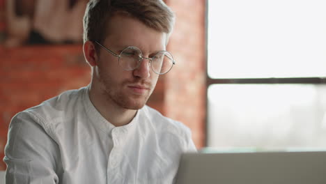 Schöner,-Ernster-Mann-Tippt-Text-Auf-Laptop-Und-Arbeitet-Ferngesteuert-Im-Café.-Nahaufnahme-Eines-Gesichts-Mit-Brille