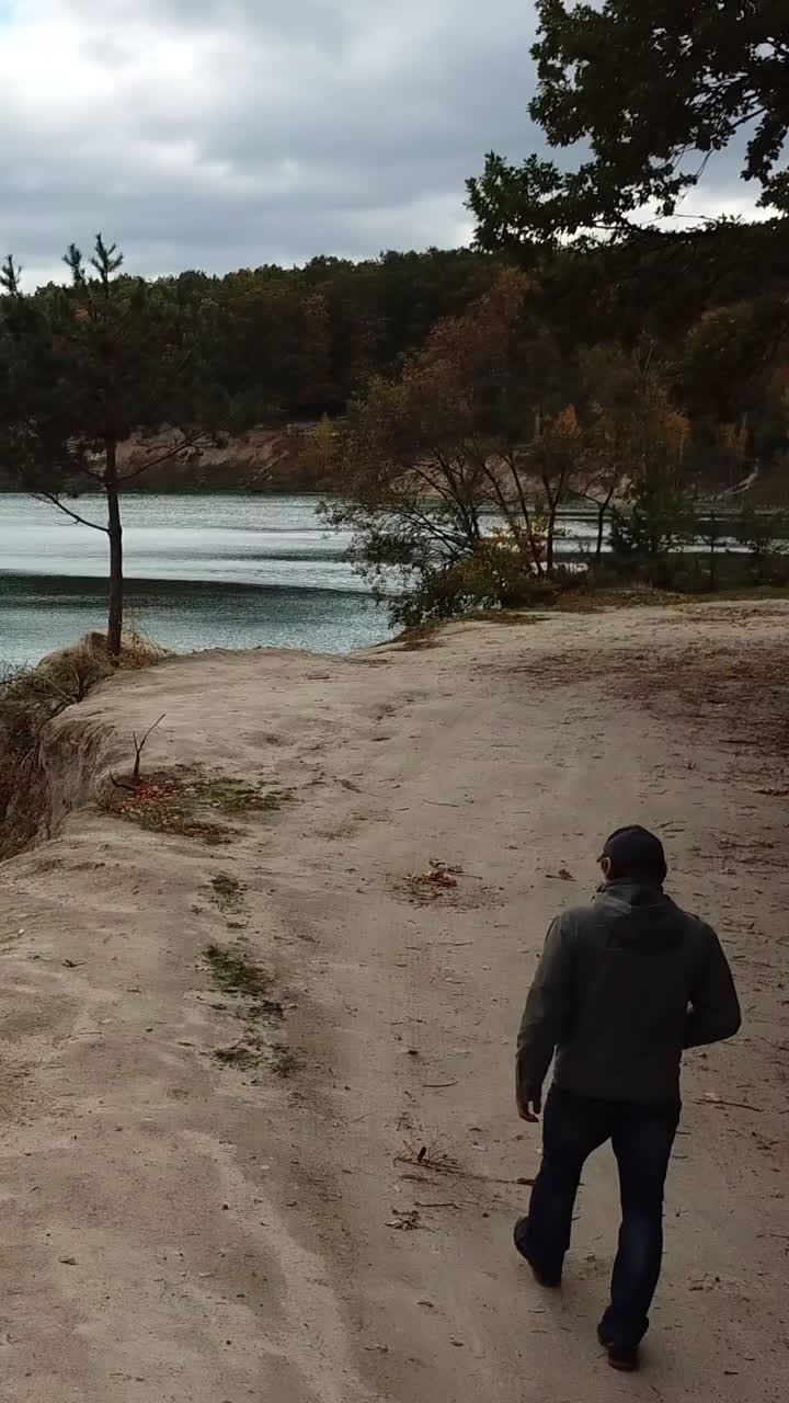 Man walking on nature. Aerial view of adult man walking near forest with lake Vertical video
