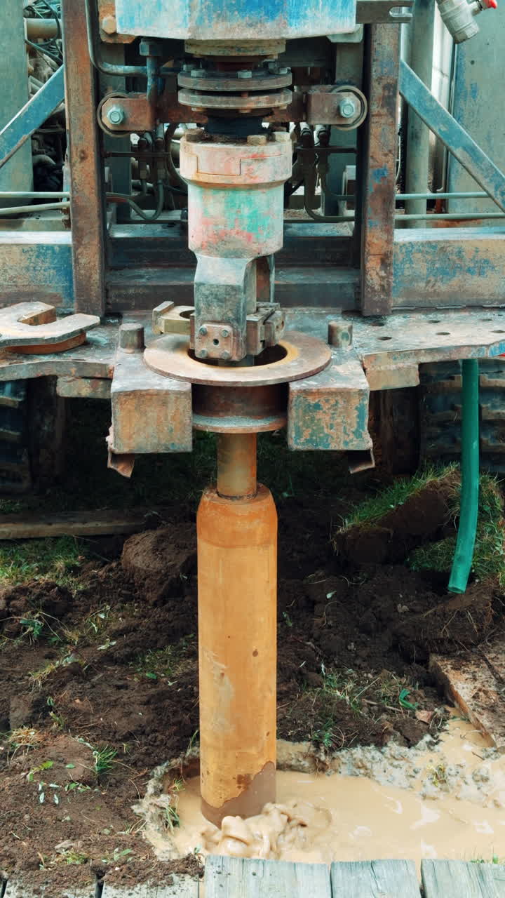 Large forcer is rotating in the muddy puddle in the ground. A shovel is helping the work of machine. Well boring process. Vertical video.