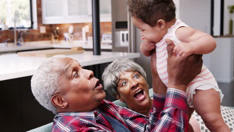 grandparents sitting on sofa playing with baby granddaughter at home