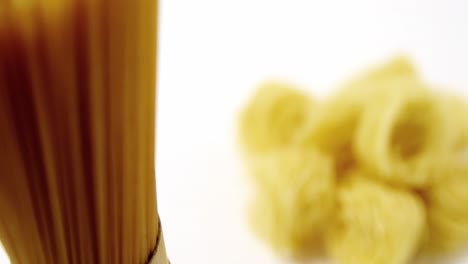 Stack-of-raw-tagliolini-pasta-and-spaghetti-held-vertically-on-white-background