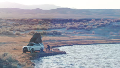 back country camping next to lake with roof top tent on car, aerial