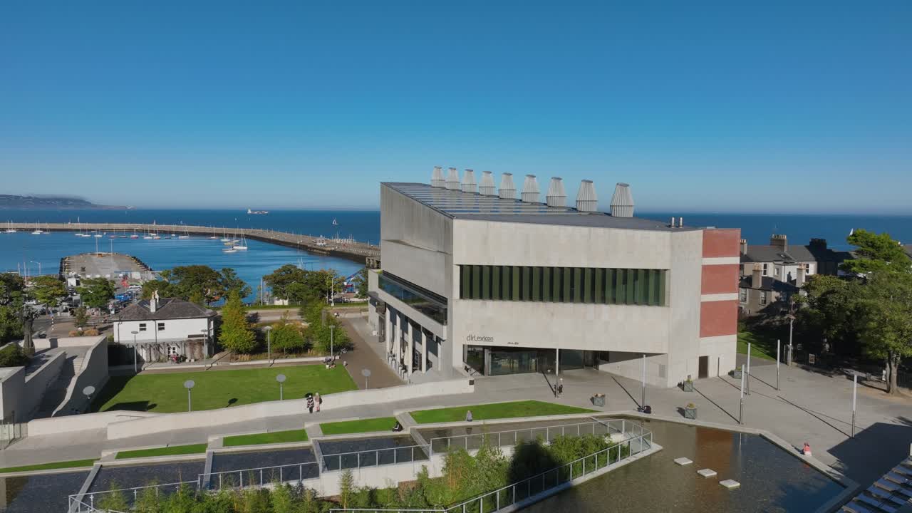 LexIcon, Dún Laoghaire, County Dublin, Ireland, September 2024. Drone descends in a gentle clockwise orbit around the sleek modern building facing Dublin Bay on beautiful day under a clear blue sky.
