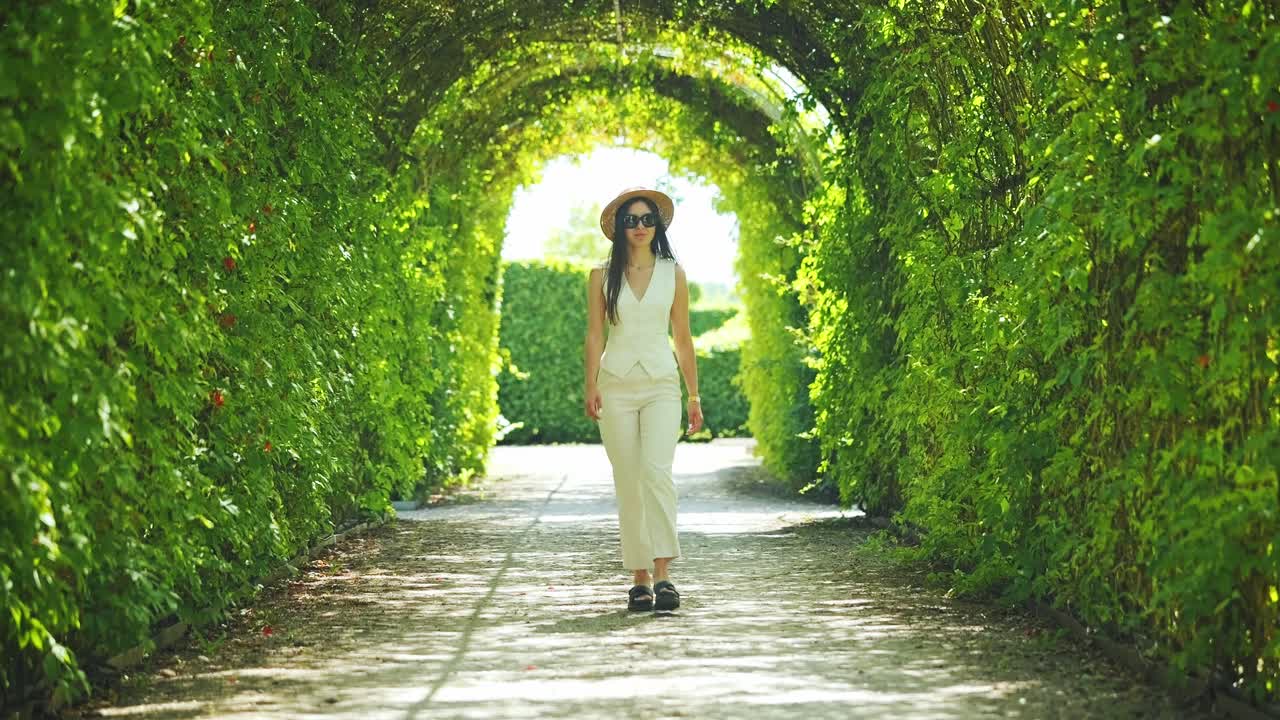 Slow motion of elegant woman walking under sunlit archway in French-style garden