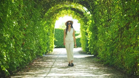 slow motion of elegant woman walking under sunlit archway in french-style garden