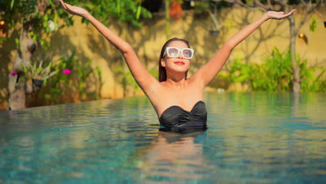 Una-Mujer-Joven-Y-Sana-En-Una-Piscina-Infinita-Levanta-Los-Brazos-Para-Saludar-Al-Sol-Y-Al-Día