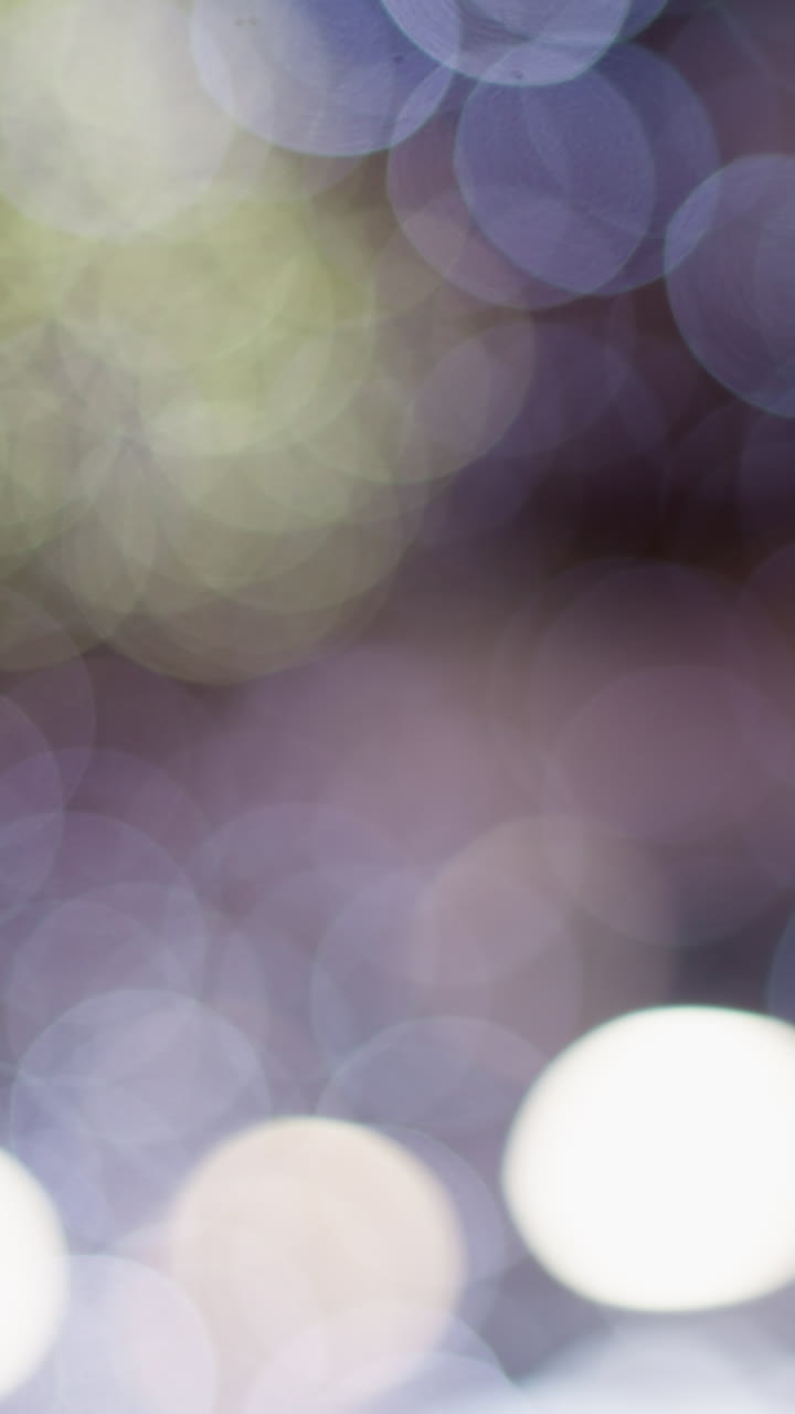 Abstract blurred bokeh effect with soft circular lights in shades of purple, white, and green, captures a dreamy, artistic visual with luminous spots creating a mesmerizing and tranquil ambiance