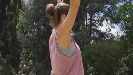 mujer caucásica sonriente con los brazos en el aire practicando yoga en el parque