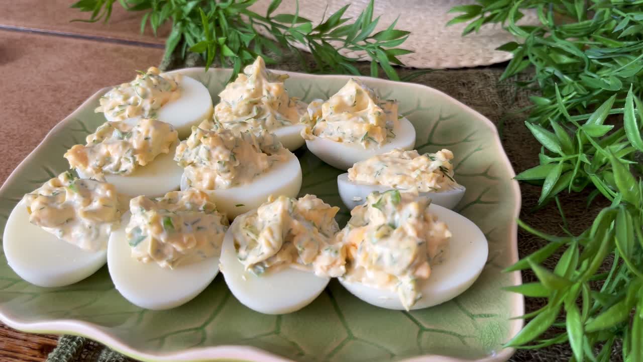 Close-up of homemade deviled eggs on a leaf-shaped platter, styled as a rustic party appetizer with creamy herb filling and fresh decorative greenery