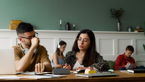 Vista-De-Cerca-De-Un-Estudiante-Con-Auriculares-Hablando-Con-Una-Compañera-En-La-Mesa