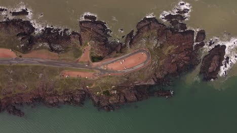 toma aérea de arriba hacia abajo de autos en el mirador de una colina rocosa rodeada por el océano en punta ballena, uruguay