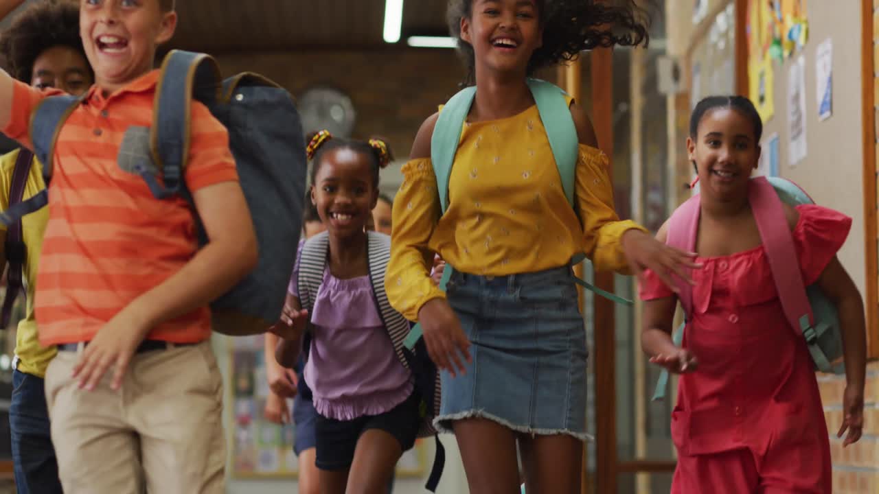 Diverse group of happy schoolchildren wearing backpacks, running fast through school corridor