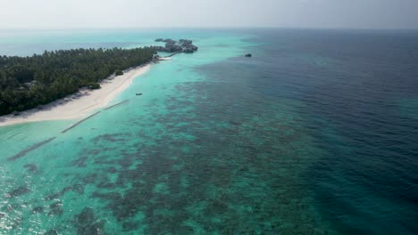 tropical reef surrounding maldives island resorts with overwater bungalows in distance