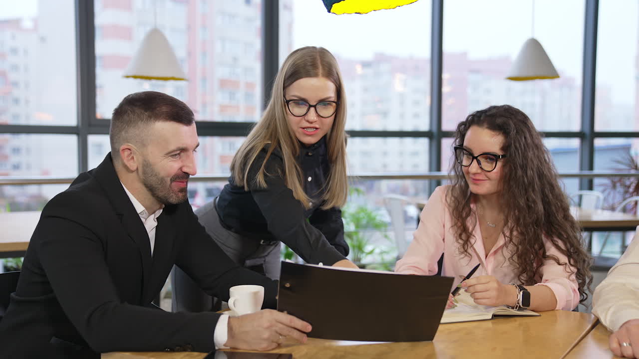 Productive teamwork in the beautiful spacious office. Long-haired lady stands leaning on table commenting papers in the boss's hands.