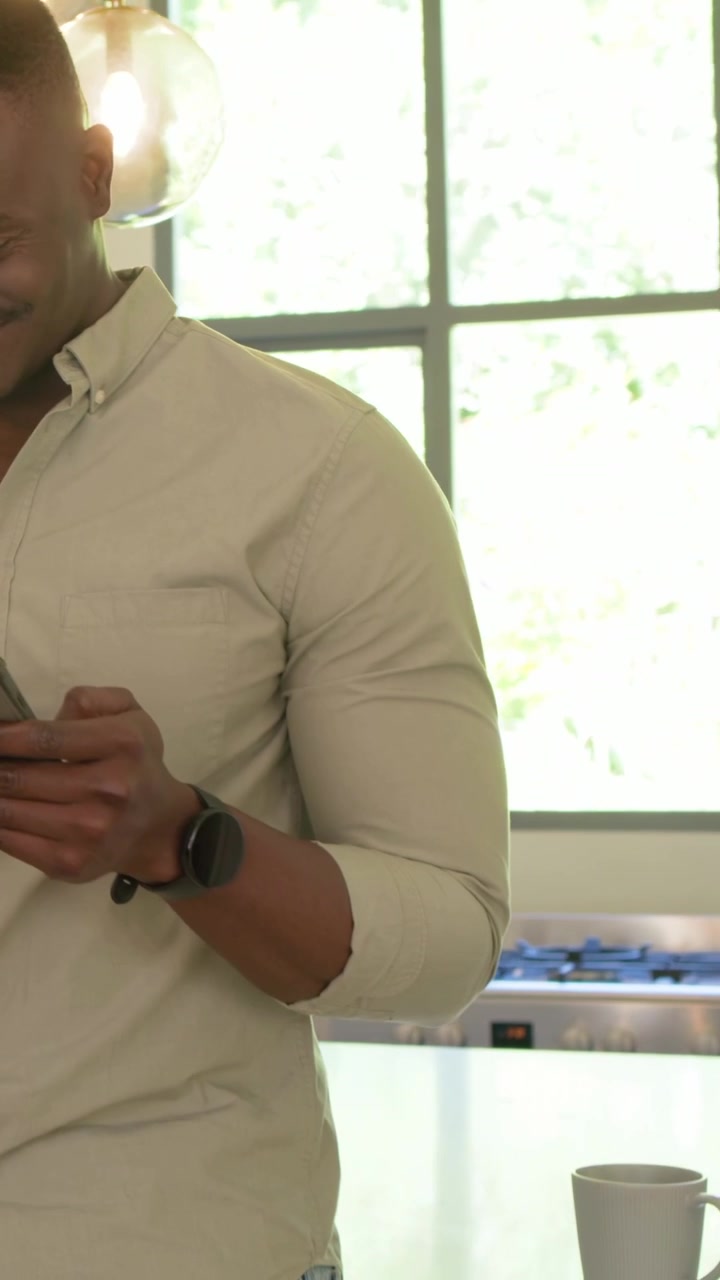 Vertical video: Holding dark tablet man tapping scrolling reading in kitchen, wearing button-up