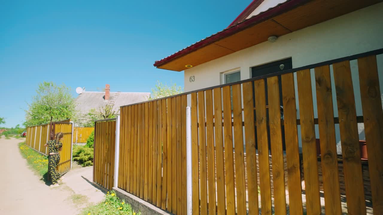 Niña linda abriendo una valla de madera amarilla frente a una casa mientras caen hojas en flor.