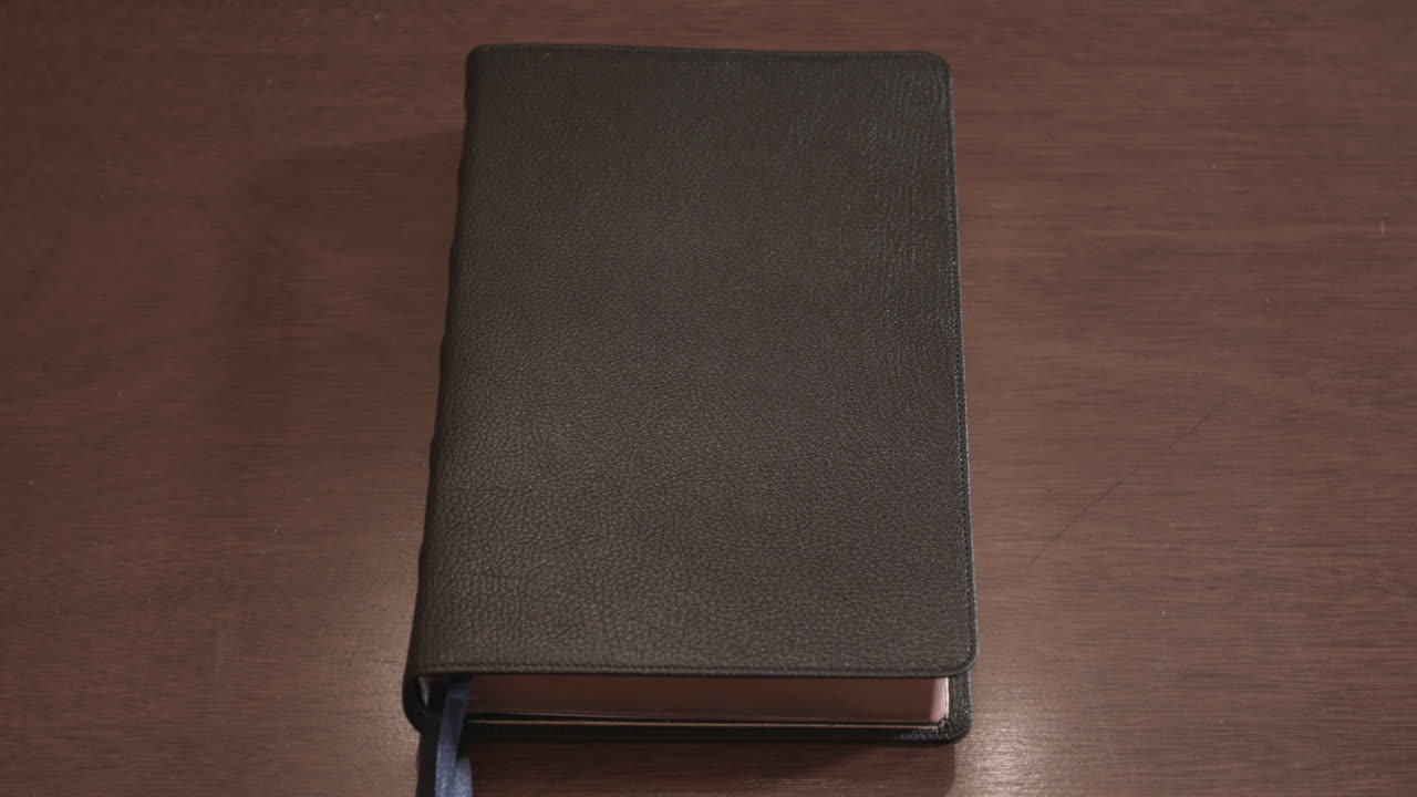 Hand opens a leather-bound holy Bible book sitting on a wood table