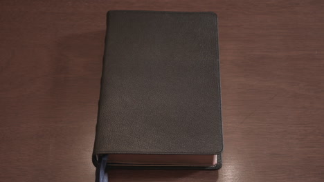 hand opens a leather-bound holy bible book sitting on a wood table