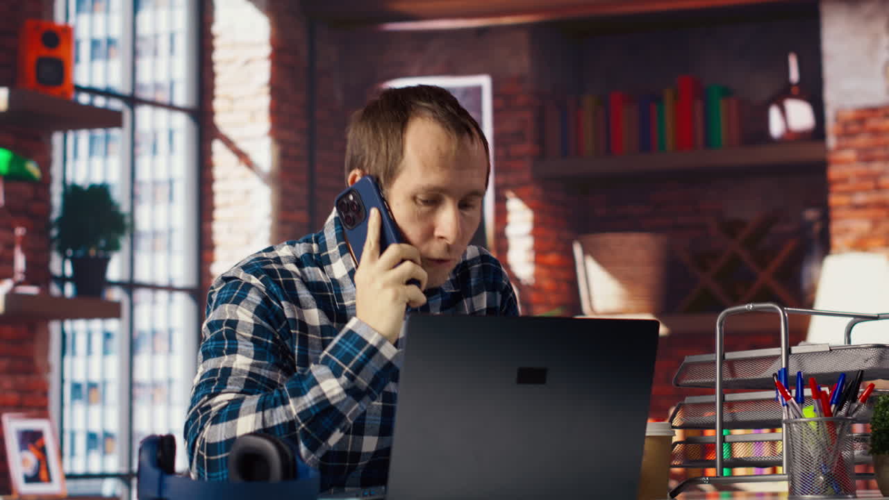 Manager in home office sitting at desk in front of laptop, calling employee