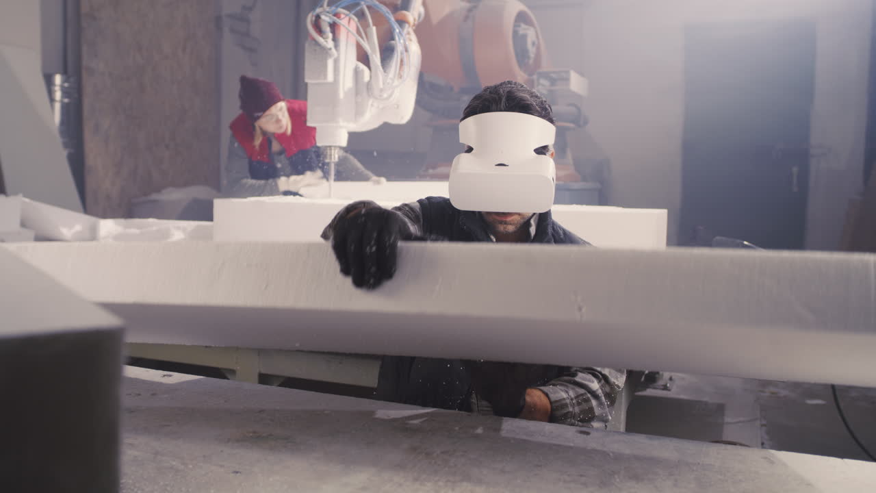 Factory worker using VR headset while operating foam cutting robot
