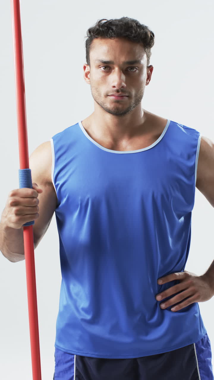 Vertical video: Holding javelin, athlete in blue sportswear posing confidently for portrait